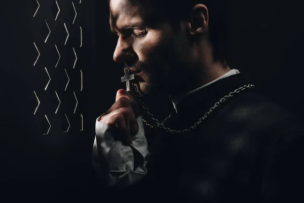 Young Tense Catholic Priest Kissing Cross His Necklace Dark Confessional — Stock Photo, Image