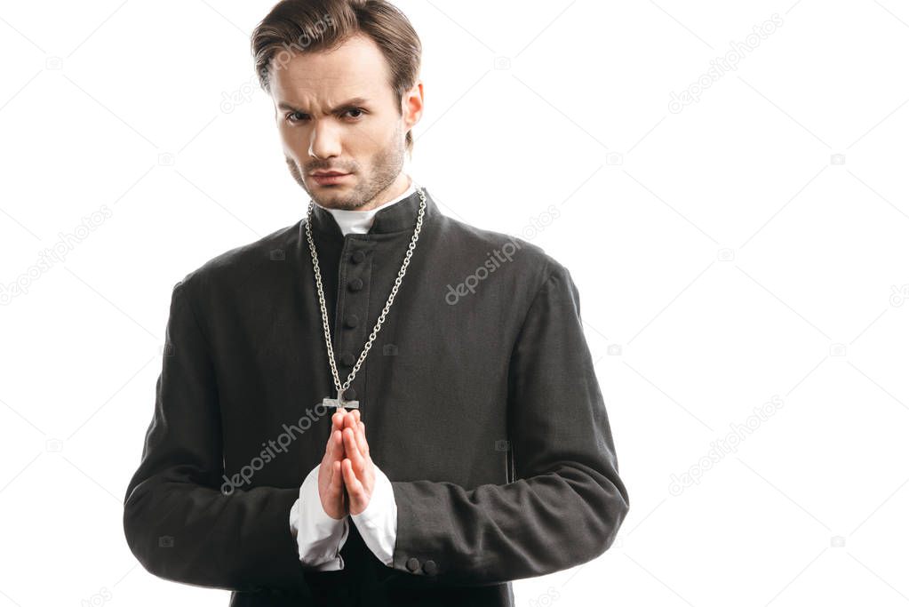 serious, strict catholic priest with praying hands looking at camera isolated on white