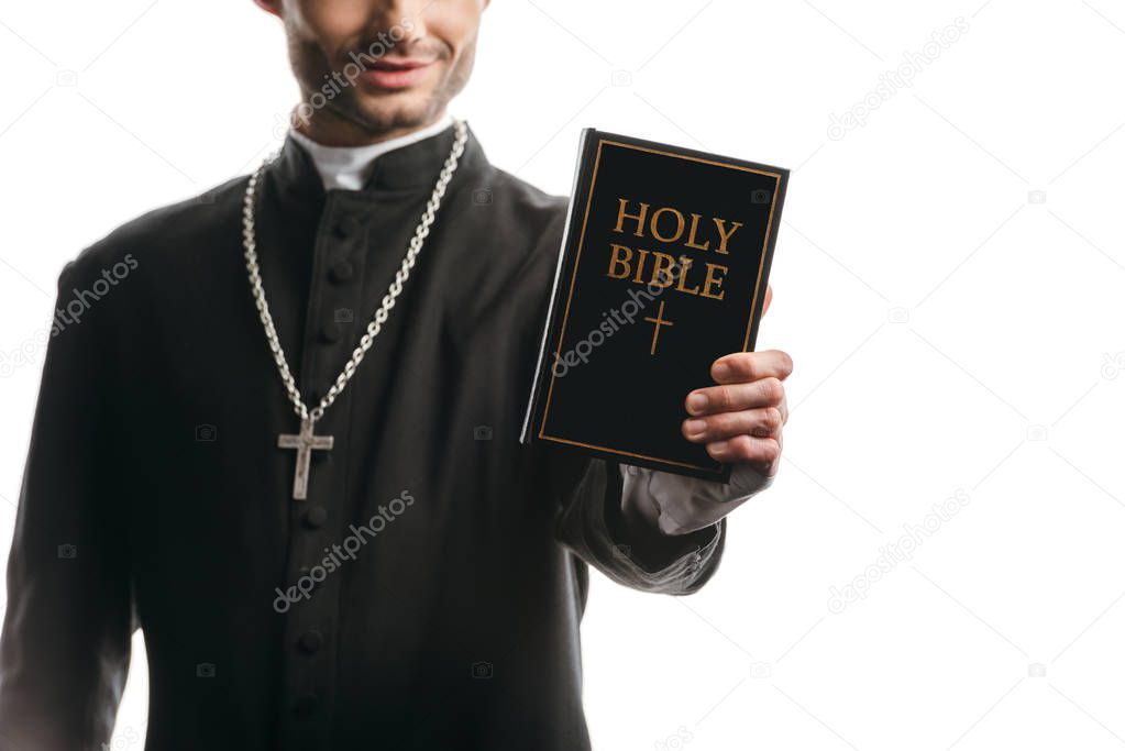cropped view of young catholic priest showing holy bible isolated on white