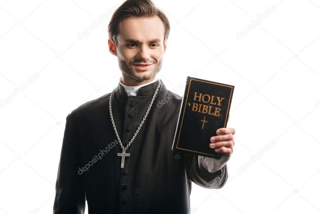 young catholic priest smiling while holding holy bible isolated on white