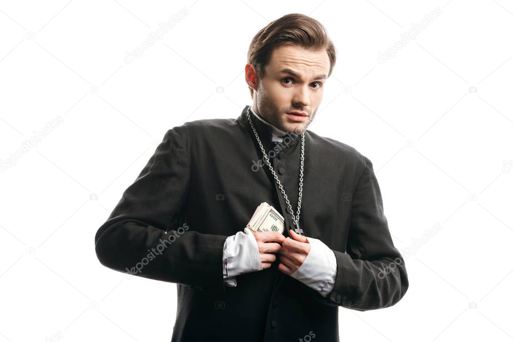 scared catholic priest looking at camera while hiding money under cassock isolated on white