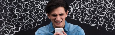 panoramic shot of worried young man using smartphone, with steam from ears drawing on chalkboard