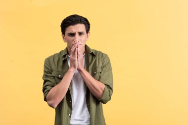 portrait of shocked young man holding hands together, isolated on yellow