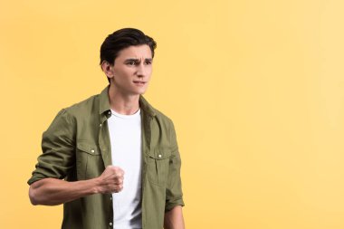 angry young man holding fist, isolated on yellow