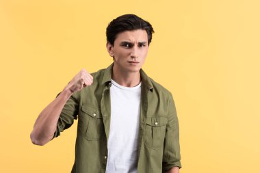 handsome angry young man holding fist, isolated on yellow