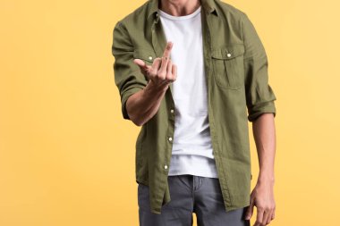 cropped view of young man showing middle finger, isolated on yellow