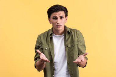 angry young man with shrug gesture, isolated on yellow
