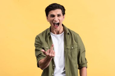 aggressive young man screaming and showing middle finger, isolated on yellow