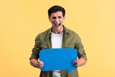 stressed man yelling and holding blue speech bubble, isolated on yellow