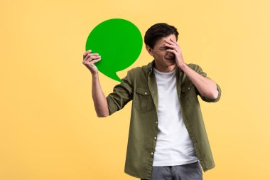 frustrated man holding green speech bubble, isolated on yellow