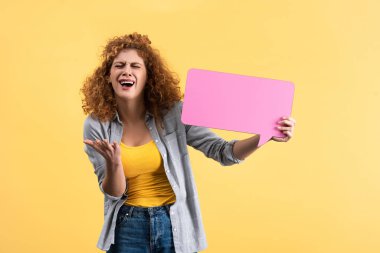 stressed crying girl holding empty pink speech bubble, isolated on yellow  
