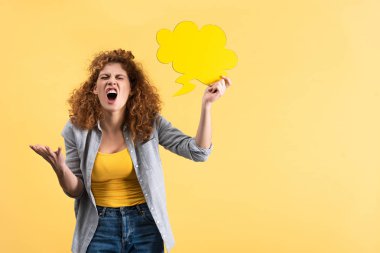 angry woman yelling and holding empty speech bubble in shape of cloud, isolated on yellow 