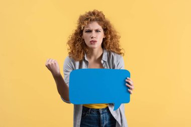 angry woman showing fist and holding empty speech bubble, isolated on yellow 