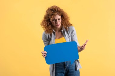 frustrated woman crying and holding empty blue speech bubble, isolated on yellow  