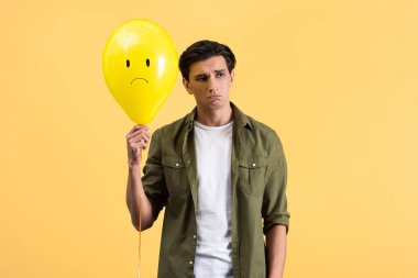 upset young man holding sad balloon, isolated on yellow clipart