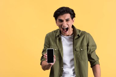 Kızgın genç adam bağırıyor ve akıllı telefonu boş ekranla gösteriyor, sarı ekranda izole edilmiş.