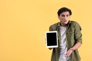 Kafası karışmış bir adam boş ekranlı dijital tablet gösteriyor, sarı ekranda izole edilmiş.