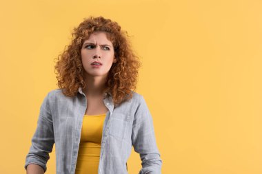confused redhead young woman, isolated on yellow