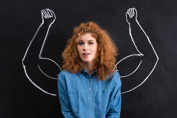 portrait of beautiful positive woman with strong muscular arms drawing on chalkboard