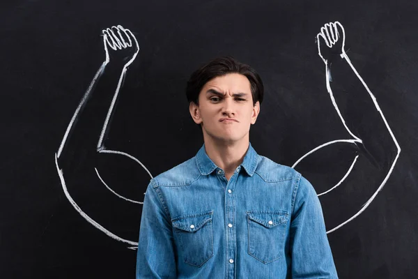 Skeptical Young Man Strong Arms Drawing Blackboard — Stock Photo, Image