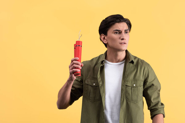 stressed young man holding dynamite, isolated on yellow