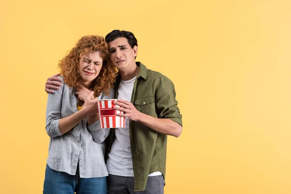 upset couple crying while watching drama movie with bucket of popcorn, isolated on yellow
