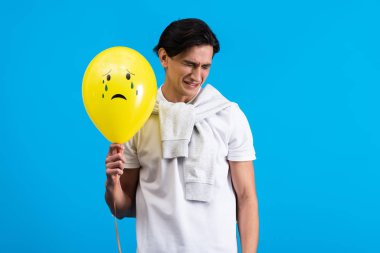 sad young man holding yellow crying balloon, isolated on blue