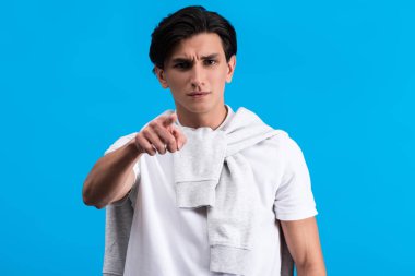 angry young man pointing at you, isolated on blue