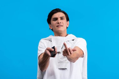 aggressive man showing middle finger while watching tv with remote controller, isolated on blue