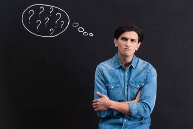 pensive young man with question marks in thought bubble on blackboard