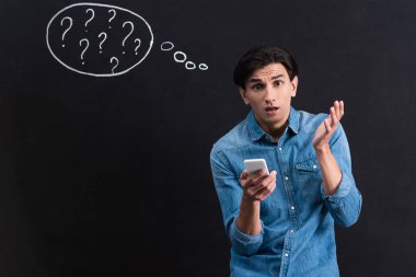Akıllı telefon kullanan şok olmuş genç bir adam. Tahtaya düşünce baloncuğu çizerek soru işaretleri çiziyor.