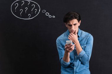 Düşünceli genç adam akıllı telefon kullanıyor. Tahtaya düşünce baloncuğu çizimleri yapıyor.