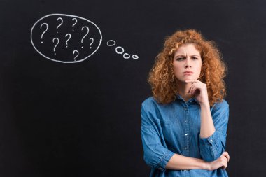 thoughtful redhead girl with question marks in thought bubble on chalkboard