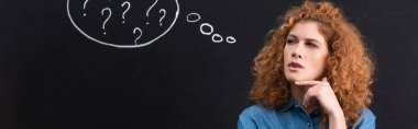 panoramic shot of beautiful thoughtful redhead girl with question marks in thought bubble on blackboard