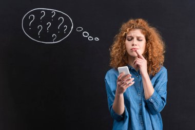 pensive woman using smartphone, question marks in thought bubble on blackboard behind 
