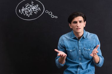 stressed young man with shrug gesture, blackboard with thought bubble drawing behind