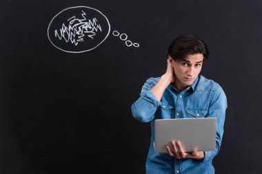 pensive young man using laptop, with thought bubble drawing on chalkboard