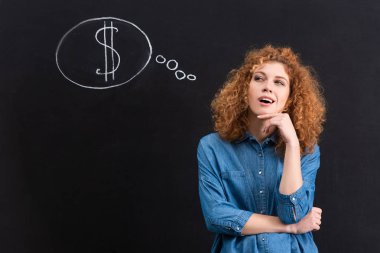 smiling thoughtful redhead girl with dollar sign in thought bubble on chalkboard
