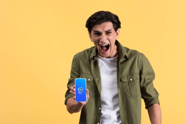 Kyiv, Ukrayna - 18 Kasım 2019: Shazam uygulamalı akıllı telefon gösteren bağıran adam sarı ekranda izole edilmiş. 