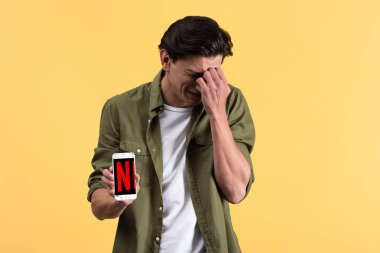 Kyiv, Ukrayna - 18 Kasım 2019: endişeli adam ekranda netflix uygulamalı akıllı telefon gösteriyor, sarıda izole edilmiş. 