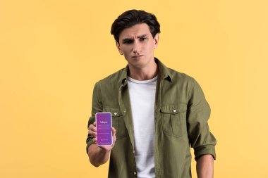 Kyiv, Ukrayna - 18 Kasım 2019: Instagram uygulamalı akıllı telefon gösteren şüpheci adam, sarı ekranda izole edilmiş. 