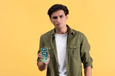 Kyiv, Ukrayna - 18 Kasım 2019: akıllı telefon gösteren yakışıklı şüpheli adam, sarıda izole edilmiş. 