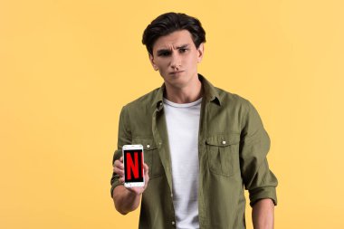 Kyiv, Ukrayna - 18 Kasım 2019: Netflix uygulamalı akıllı telefon gösteren şüpheci adam, sarı ekranda izole edildi 