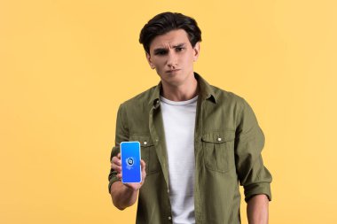 Kyiv, Ukrayna - 18 Kasım 2019: Shazam uygulamalı akıllı telefon gösteren şüpheci adam, sarı ekranda izole edilmiş. 