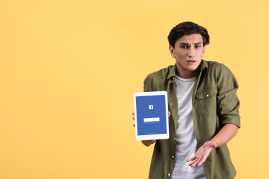 Kyiv, Ukrayna - 18 Kasım 2019: omuz silkme hareketli duygusal adam facebook uygulamalı dijital tableti ekranda gösteriyor, sarıda izole edilmiş. 