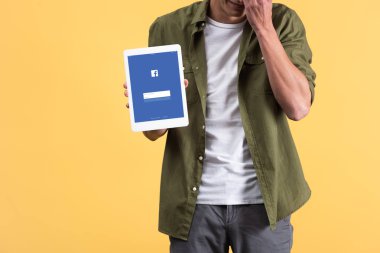 Kyiv, Ukrayna - 18 Kasım 2019: Ekranda Facebook uygulamalı dijital tablet gösteren adamın görüntüsü, sarı üzerine izole edilmiş 