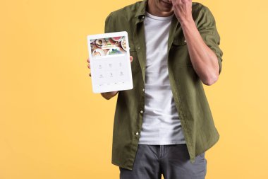 Kyiv, Ukrayna - 18 Kasım 2019: Ekranda dört kare uygulamalı dijital tablet gösteren, sarı üzerine izole edilmiş bir adam görüntüsü 