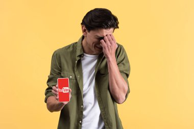 Kyiv, Ukrayna - 18 Kasım 2019: ekranda youtube uygulaması ile akıllı telefon gösteren ağlayan adam, sarı ekranda izole edilmiş.