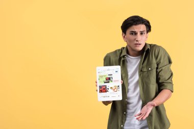 Kyiv, Ukrayna - 18 Kasım 2019: omuz silkme hareketli duygusal adam dijital tableti ekranda ebay uygulaması ile gösteriyor, sarı ekranda izole edilmiş. 
