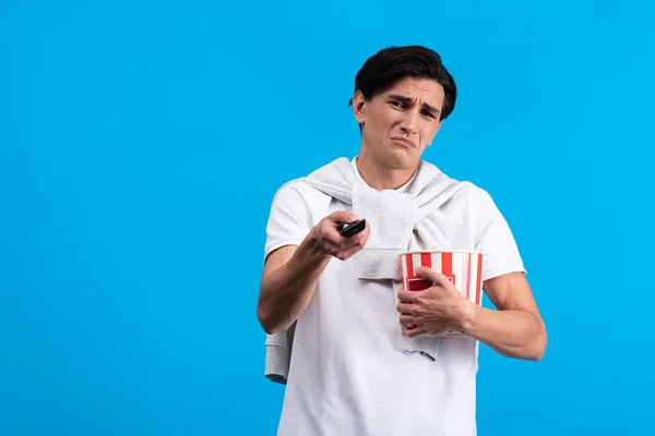 Sad Young Man Watching Remote Controller Popcorn Isolated Blue — Stockfoto
